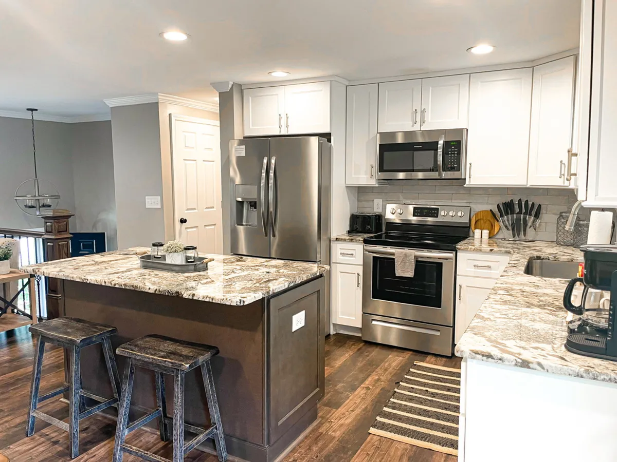 A modern kitchen with an island countertop, stainless steel appliances, wooden stools, and backsplash tiles. The scene is lively and social—perfect for cooking, entertaining, and spending quality time during longer stays.