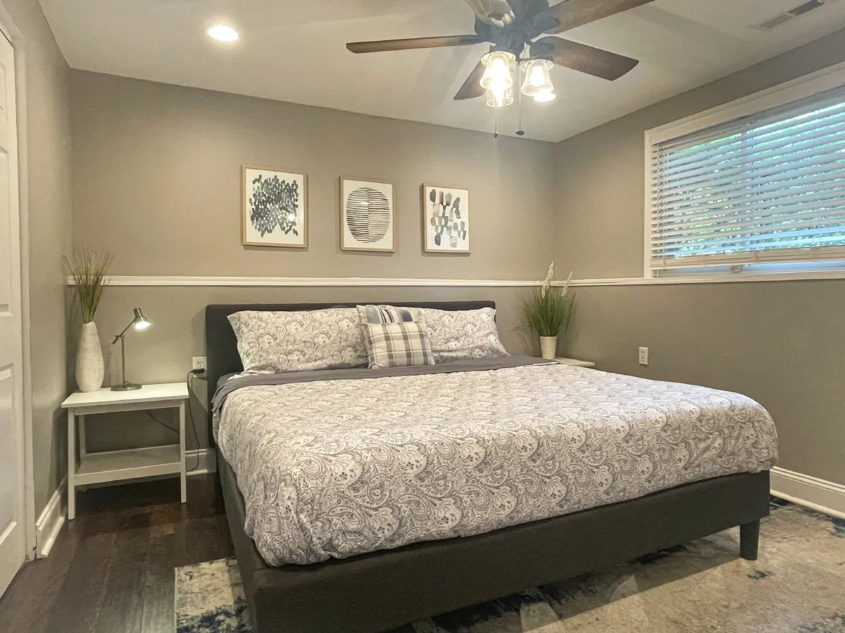 A cozy bedroom with a queen-sized bed adorned with patterned bedding, decorative wall art, and a nightstand with a lamp. The soft light creates a peaceful, relaxing atmosphere.