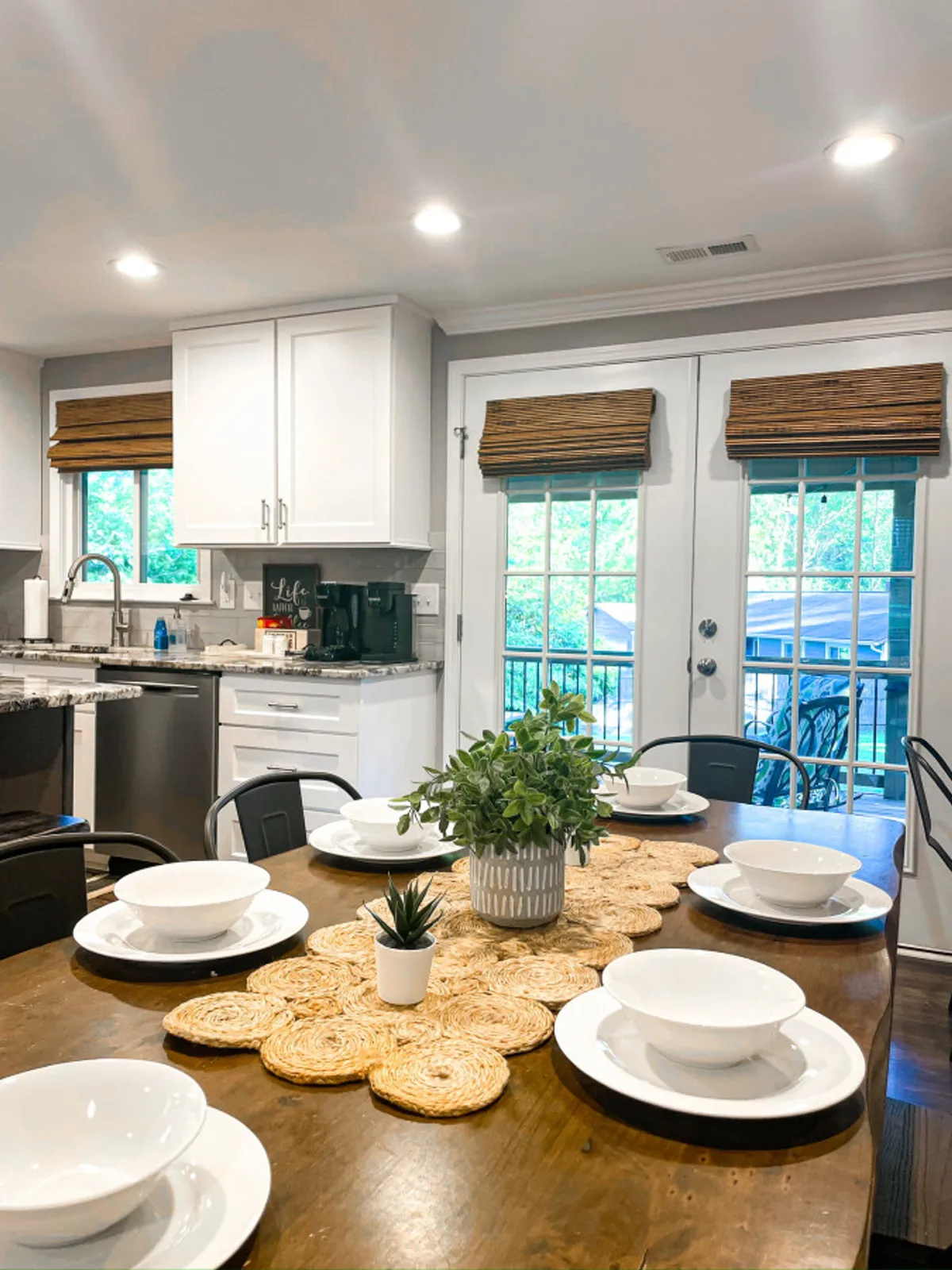 A welcoming dining area with a dining table, bowls, green plant, kitchen cabinets, and large windows. The space is bright, inviting, and ideal for family meals, cooking together, or entertaining guests—the kinds of daily comforts and rituals that help guests feel at home during longer stays.