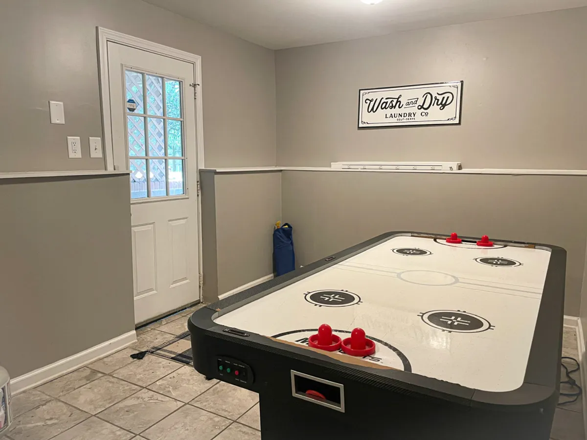 A laundry area that includes an air hockey table, doorway, and a laundry sign, merging fun and practicality. The space appears bright and functional, suitable for extended stays.