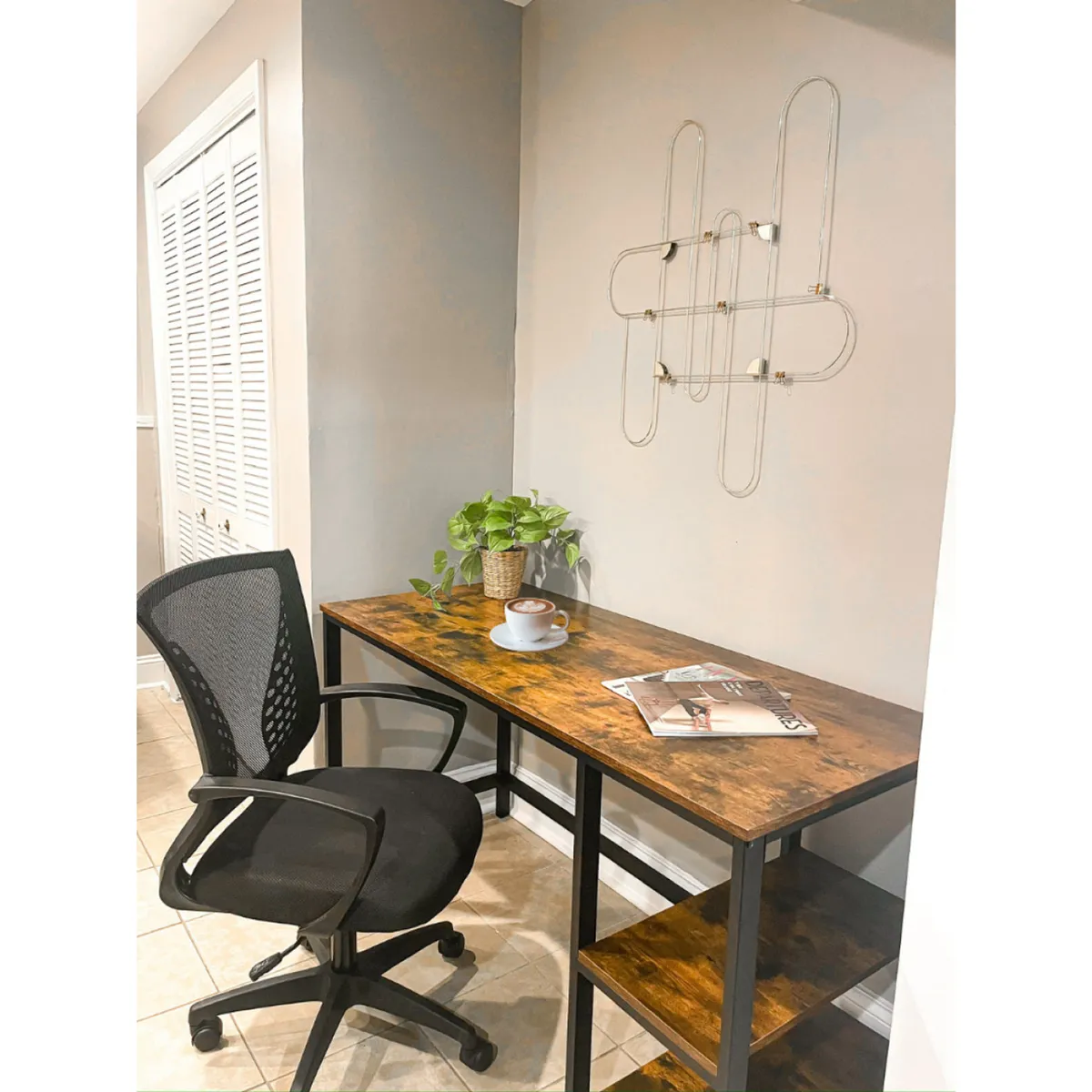 A modern, productive workspace with a wooden desk, black chair, green plant, coffee cup, magazines, and wall art. The setup suggests a quiet, focused environment—ideal for guests needing to work remotely or stay productive during their business trip.