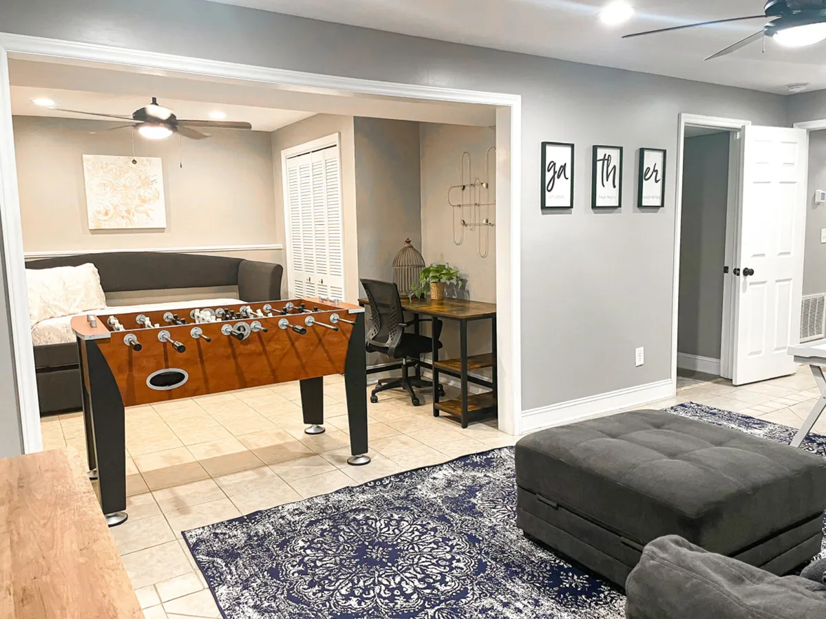 The photo showcases a foosball table with a cozy seating area, a desk accessorized with plants, and decorative wall art. The setup is playful yet comfortable, ideal for socializing, working, or engaging in friendly competition.